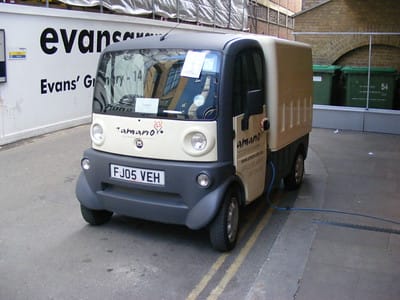 Photo of an small electric van, with a charging cable running offscreen. 